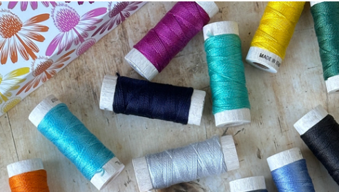 Aurifil cotton thread spools in blue, green, yellow, pink and grey on a table