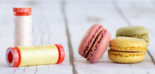2 Aurifil thread spools 50 weight, white and yellow, with 3 macaron sweets in candy colours
