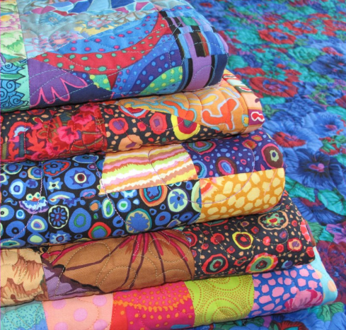 An image of a very colourful stack of quilts made with Kaffe Fassett fabrics